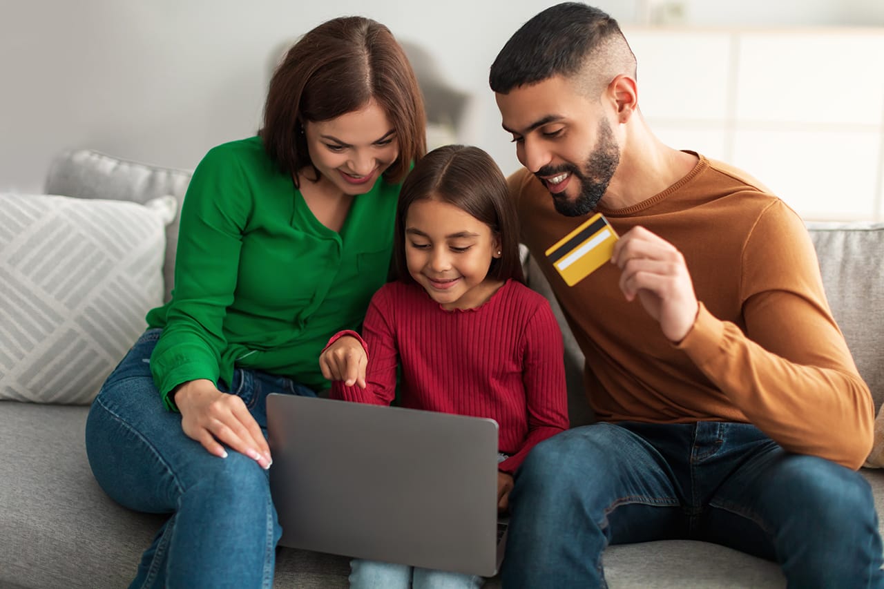 A family of three with a small girl that are sitting in front of a laptop, browsing through an eCommerce website